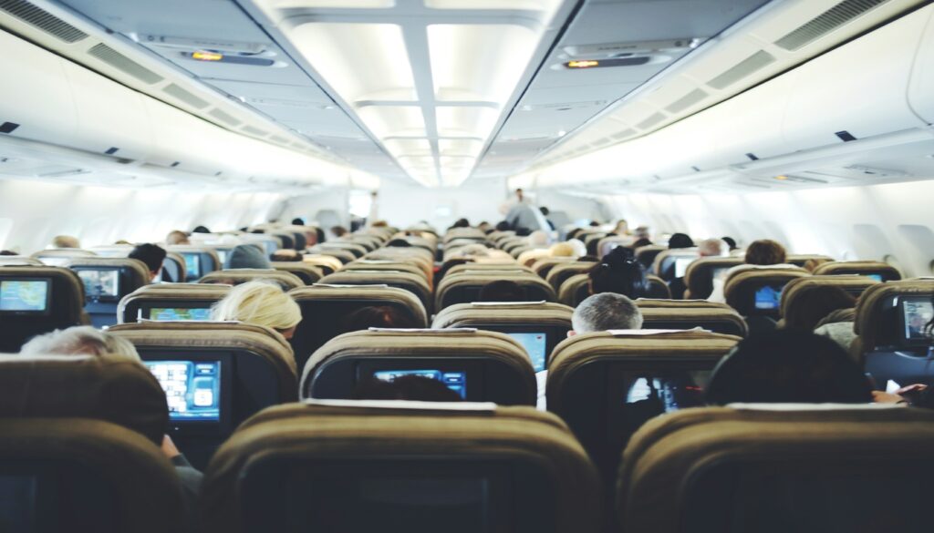Airplane cabin interior with passengers watching seatback screens on Boston to Miami flights
