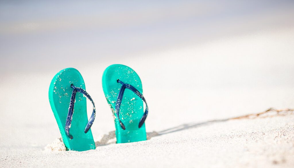 Turquoise flip-flops on sandy beach evoking relaxation after Boston to Miami flights