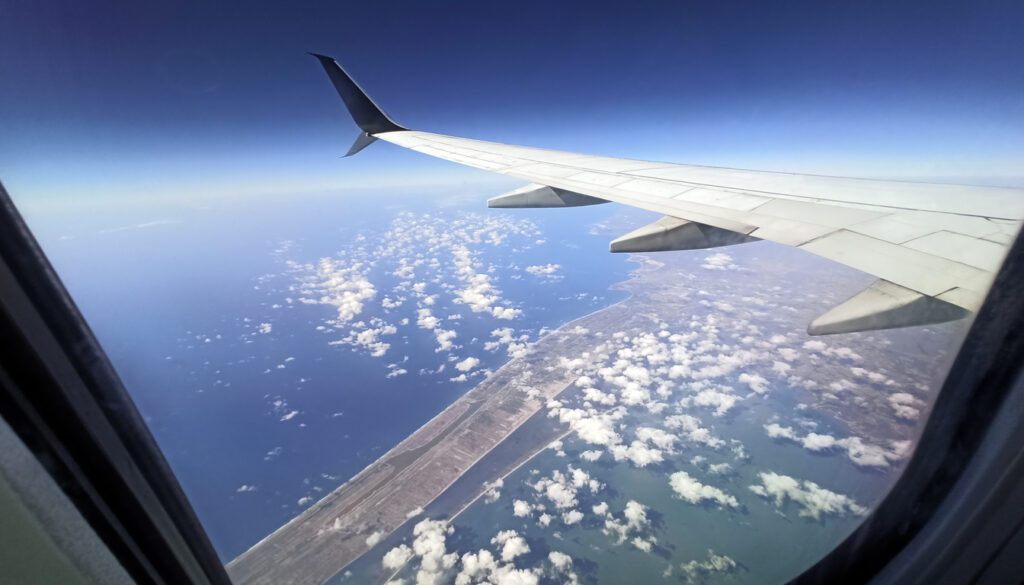 Aerial view from airplane window showing wing over ocean and clouds on Boston to Miami flights