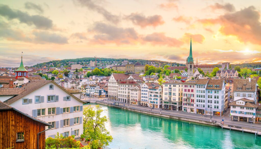 Scenic sunset view of Zurich along the Limmat River, showcasing historic buildings and church spires – one of the best cities to visit in Switzerland.