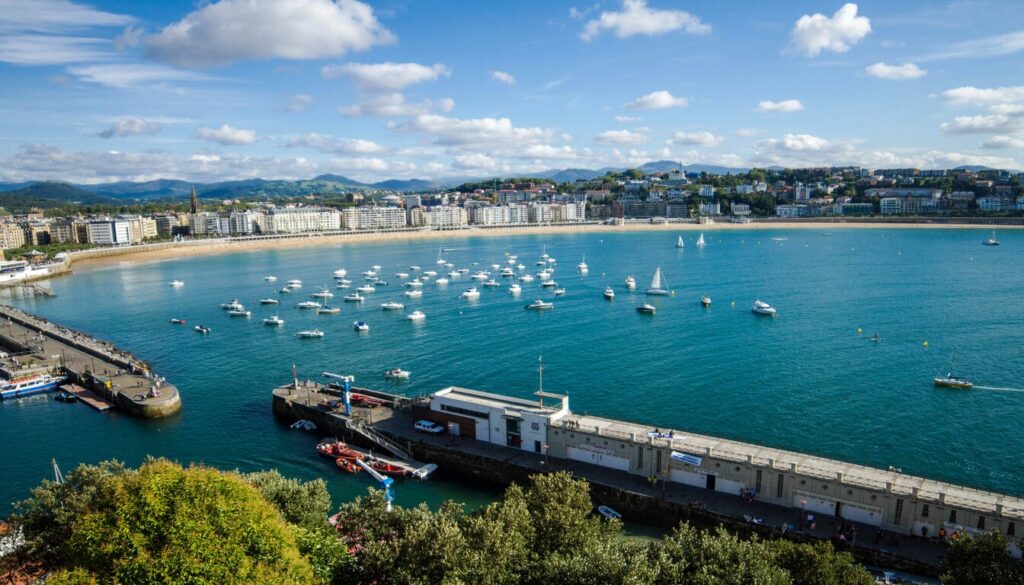 Aerial view of La Concha Beach in San Sebastián, with boats in the clear water and the scenic city skyline along the bay, recognized as one of the best beaches in Spain.