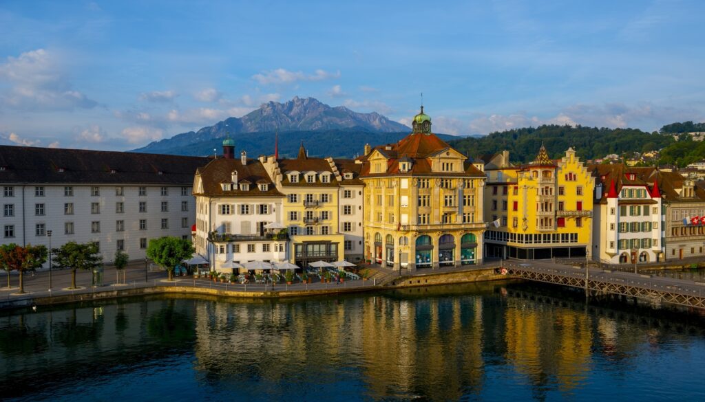 Best city to visit in Switzerland - scenic view of Lucerne with colorful buildings, river, and mountains.