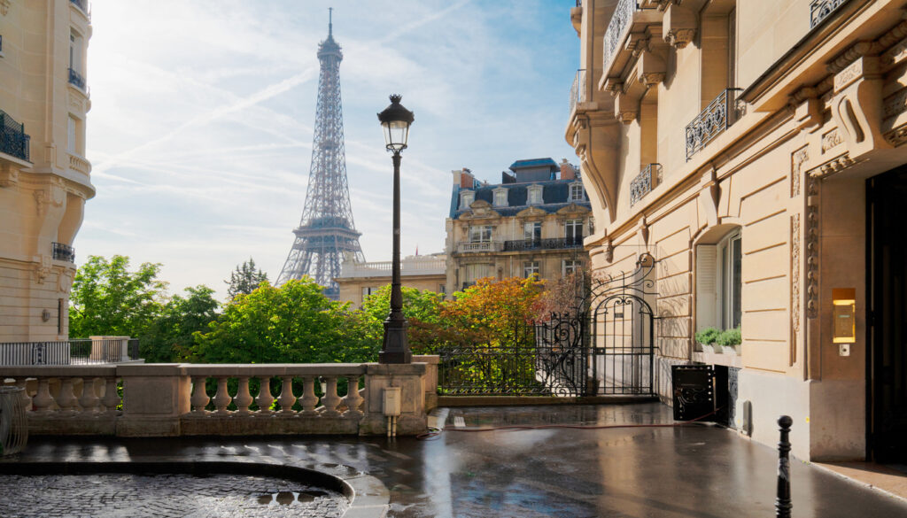 Hotels in Paris with Eiffel Tower view — charming Parisian street and luxury hotel entrance overlooking the Eiffel Tower on a sunny morning.