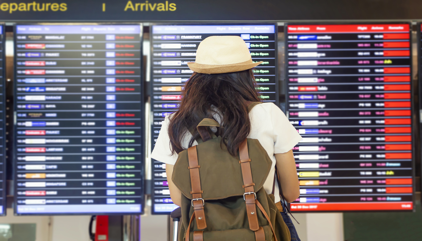 flights from usa to venice italy options woman with a backpack is looking at a flight departure board in an airport, scanning available flights. The board lists several destinations and flight information, including flights to Venice Italy.