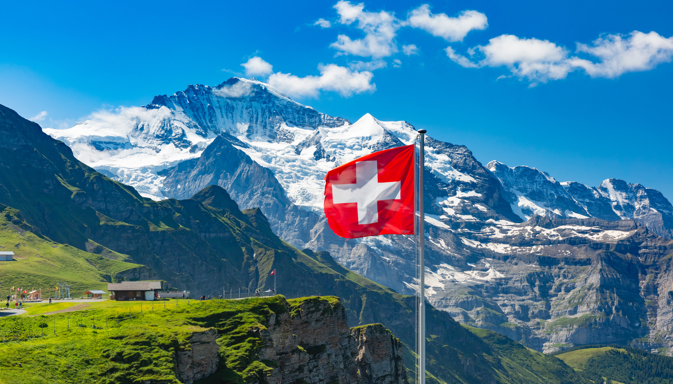 Swiss flag waving with stunning alpine mountains in the background — best time to travel to Switzerland.