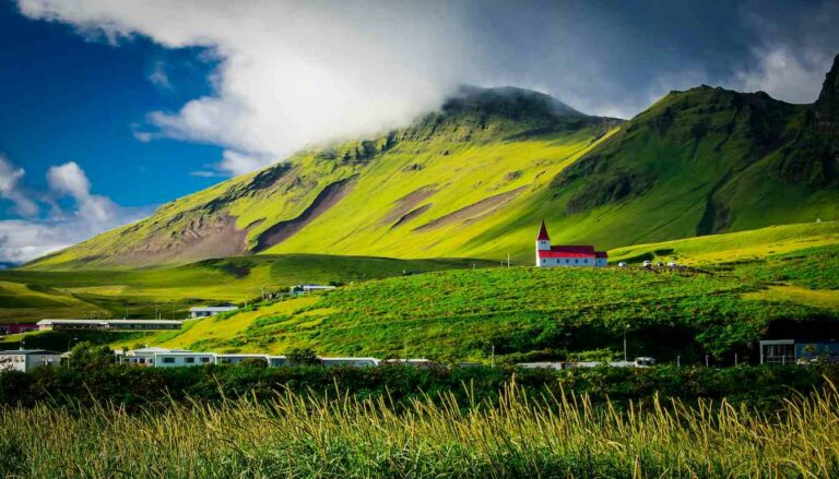 Scenic view of green mountains and a red-roof church in Iceland during summer, best time to visit Iceland